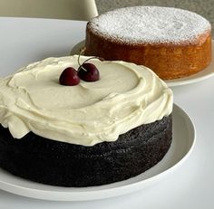 two cakes sitting on top of white plates next to each other, one with frosting and the other topped with cherries