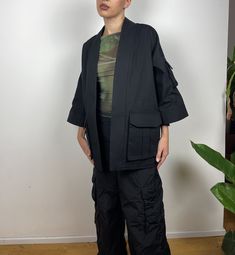 Black Kimono with utility-style cargo pockets. The oversized design is great for layering over jackets, coats and jumpers. It is designed with  ¾ length sleeves and an open front. Made from high-quality sanded canvas from a historic UK company. All fabrics used are 100% plastic-free. This item comes in XS, S, M and L sizes. Please specify which size you would like upon purchase.  Made in East London, UK. Solid Utility Jacket With Multiple Pockets, Casual Oversized Outerwear With Roll-up Sleeves, Fall Utility Outerwear With Roll-up Sleeves, Modern Workwear Outerwear With Multiple Pockets, Black Utility Outerwear With Cargo Pockets, Modern Multi-pocket Work Outerwear, Solid Techwear Outerwear With Cargo Pockets, Oversized Blazer With Pockets, Black Utility Jacket With Patch Pockets For Spring