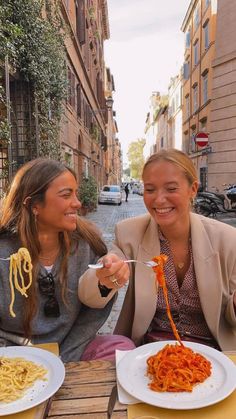 two women sitting at an outdoor table eating spaghetti