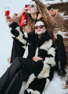 two people dressed in costumes are sitting on the snow with wine glasses and one is holding a bottle