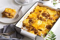 a casserole dish with meat and cheese in it on a table next to a cup of coffee