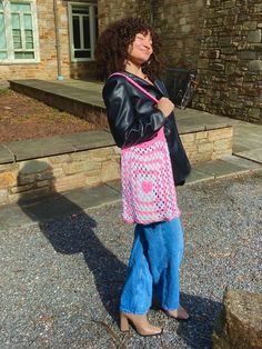 a woman standing in front of a building with a pink and white bag on her shoulder