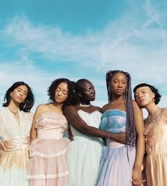 four women standing together in dresses against a blue sky