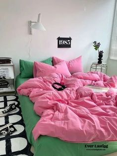 a bed with pink and green comforters in a white room next to a black and white rug