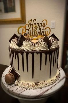 a birthday cake with white frosting and chocolate drizzled on top, sitting on a table