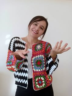 a woman wearing a colorful crochet jacket and holding her hands out to the side