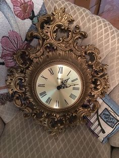 an ornate gold clock sitting on top of a couch next to a wall hanging sign