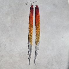 Celebrate fall with these statement earrings, in vibrant shades of red, orange, gold, and silver. Inspired by sunsets, candy corn, changing leaves, Halloween, and everything in between, these long earrings have a dynamic fringe design that catches light and adds movement to your look. Perfect for those who love bold, seasonal accessories, these earrings are as eye-catching as a fall sunset. (also available in sizes Medium (5.75 in.) and Small (3 in.)) Size of beaded portion: 7.75 in. x .5 in. Fall Sunset, Sunset Boulevard, Changing Leaves, Orange Gold, Candy Corn, Shades Of Red, Long Earrings, Gold And Silver, Statement Earrings