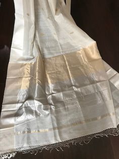 This is a beautiful handloom off-white maheswari silk by cotton saree with beautiful diamond shaped sona roopa booties, silk borders and tisuue pallu with gold and silver stripe zari in pallu. Saree is finished with tassels. Sarees comes with a plain unstitched blouse piece with borders similar to the saree. Falls and pico are already done. Colours may vary slightly depending upon the lighting and individual device settings. Dry clean only All sales are final. Handloom products may have some irr White Tussar Silk Traditional Wear With Border, Traditional White Tussar Silk Wear With Border, Off White Tussar Silk Dupatta With Pallu, White Silk Dupatta With Border, Festive Off-white Handloom Dupatta, White Handloom Cotton Silk Saree, White Cotton Silk Handloom Saree, White Silk Handloom Dupatta, White Raw Silk Saree With Border