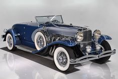 an antique blue car is parked on a reflective surface in front of a white background