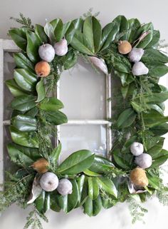 a wreath is hanging on the wall next to an old window with fruit and leaves