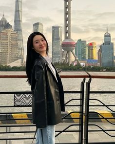 a woman standing in front of a body of water next to a cityscape