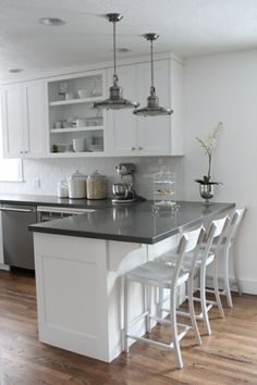 a kitchen with white cabinets and black counter tops is pictured in this image, there are four bar stools at the center of the island