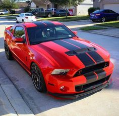 a red and black mustang parked on the side of a road next to a house