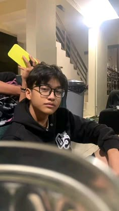 a young man sitting in front of a laptop computer while wearing glasses and holding a yellow object