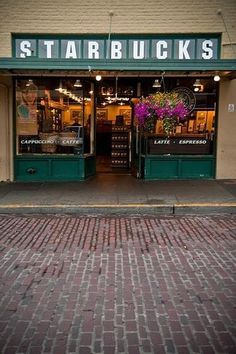 a store front with flowers in the window and brick sidewalk on one side that leads up to it