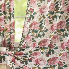 a pink flowered curtain hanging in front of a window next to a potted plant