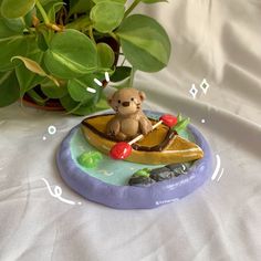 a small teddy bear sitting in a boat on a table next to some green plants