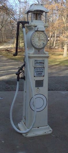 an old fashioned gas pump on the side of the road with trees in the background