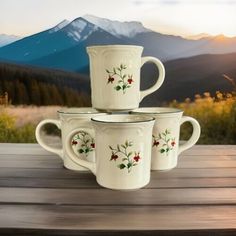 four coffee mugs sitting on top of a wooden table with mountains in the background