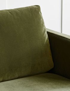 a green couch with two pillows on it's back and one pillow that is folded over