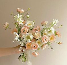 a person holding a bouquet of flowers in their hand with white and peach colors on it