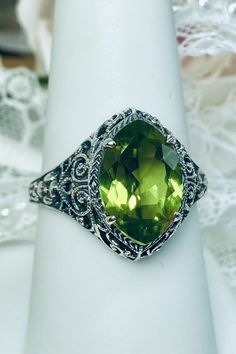 Natural Green Peridot Ring Iris Design#201 Custom Made This is a stunning Art Deco vintage reproduction ring in sterling silver filigree with a 3.12 carat Natural green peridot gemstone. The brilliant natural gem is 13mm in long by 9mm wide. The ring is 17mm North-South on the finger. The inside of the band is marked 925 for solid sterling silver. This is a lovely reproduction of a vintage antique filigree ring. There is beautiful craftsmanship evidenced in the silver filigree setting. See the f Green Jewelry With Round Cut Accent Stones, Green Center Stone Fine Jewelry Gemstones, Classic Green Gemstone With Center Stone, Green Oval Emerald Ring With Diamond Cut, Oval Green Emerald Ring With Diamond Cut, Oval Emerald Ring With Diamond Cut In Green, Elegant Peridot Gemstones For Anniversary, Elegant Peridot Gemstones For Gifts, Elegant Peridot Gemstone Gift