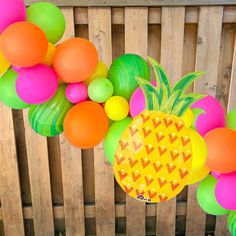 a pineapple and neon colored balloons are hanging from a wooden fence