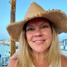 a woman wearing a straw hat on top of her head in front of the ocean