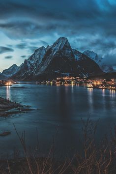 the mountains are lit up at night with lights shining on them and water in the foreground