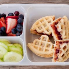 a plastic container filled with fruit and waffles on top of a wooden table