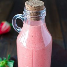 a glass bottle filled with pink smoothie next to strawberries