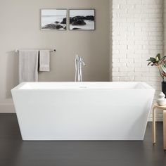 a white bath tub sitting in a bathroom next to a wooden table and two pictures on the wall