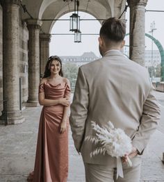 a man and woman standing next to each other in front of an archway with columns