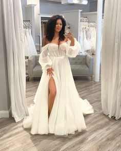 a woman taking a selfie in front of a mirror wearing a white gown with thigh high slit