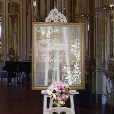 a wedding sign with flowers on it in front of a piano and chandelier