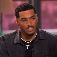 a man with a cross on his chest smiles at the camera while wearing a black shirt