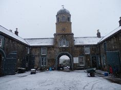 an old stone building with a clock tower in the background and snow falling on the ground