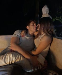 a man and woman are sitting on a couch in front of a buddha statue at night