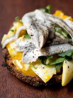 an open face sandwich topped with cheese and spinach leaves on a wooden table top