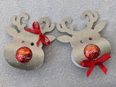 two silver reindeer ornaments with red bows on them, one has a candy bar in the shape of an antlers