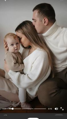 a man and woman holding a baby in their arms while they are sitting on a couch