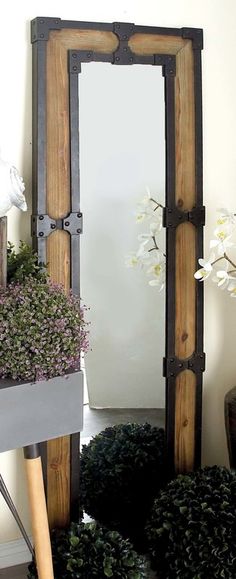 a mirror sitting on top of a wooden shelf next to flowers and potted plants