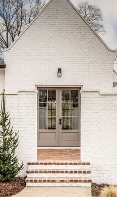 a white brick house with two doors and steps leading up to the front door