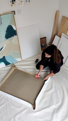 a woman laying on top of a bed next to a painting and cutting it with scissors