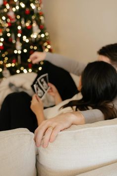 a man and woman laying on a couch next to a christmas tree