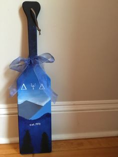 a wooden door hanger with a mountain scene painted on it and a blue ribbon tied around the top