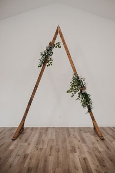 an arch made out of wooden sticks with greenery growing on it in the middle of a room