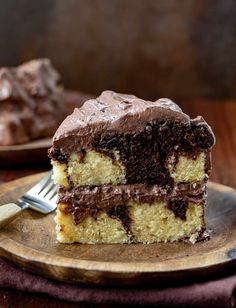 a piece of cake with chocolate frosting on a wooden plate next to a fork