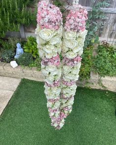 two pink and white flowers are hanging from a string in the grass next to a fence